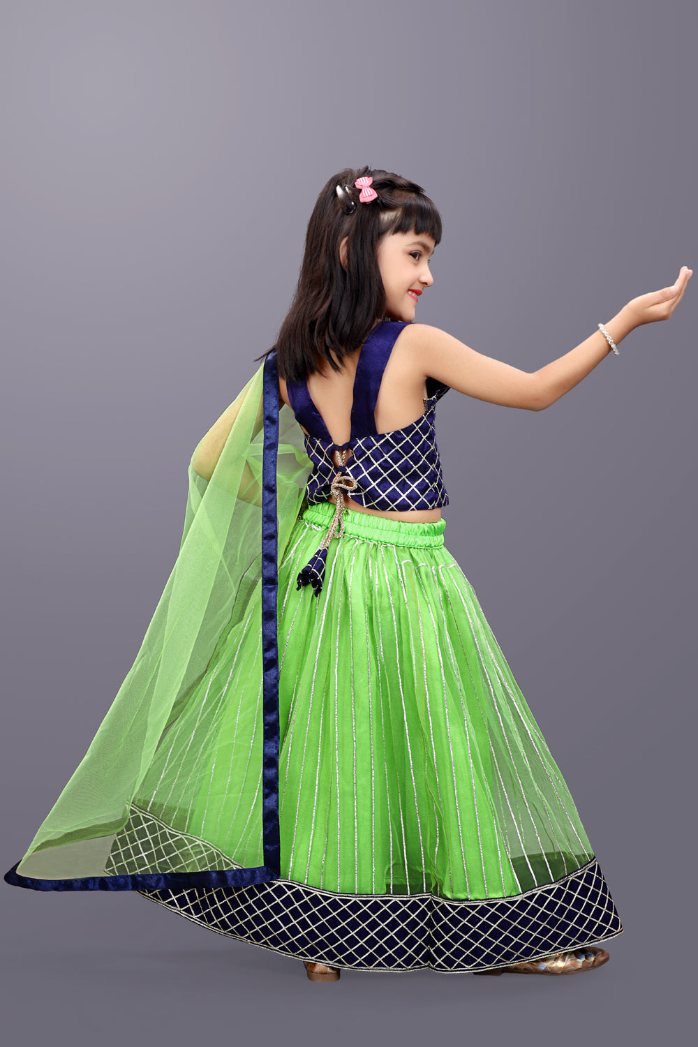 Young girl in a green and navy traditional outfit on a gray background